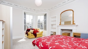 Une chambre avec un grand lit, un fauteuil, une cheminée et une vue sur l’extérieur.