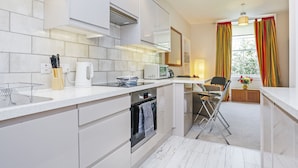 Une cuisine moderne avec des meubles blancs, un four encastré et un four à micro-ondes. On y trouve également un coin repas avec une chaise et une petite table.