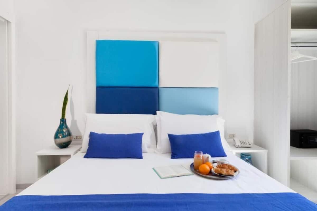 Habitación de hotel con cama, mesita de noche con teléfono y florero, y bandeja con cosas para el desayuno.