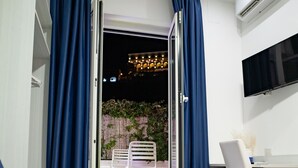 Et hotelværelse med seng, skrivebord og fjernsyn. Der er en balkon med stole og bord, samt en aircondition på væggen.