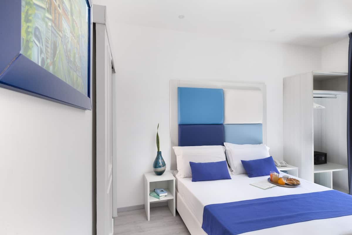 Una habitación de hotel moderna con una cama grande, una mesita de noche, un armario y un cuadro en la pared.