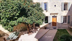 Un bâtiment en pierre avec une porte en bois, une fenêtre avec des volets et un arbre aux feuilles vertes.