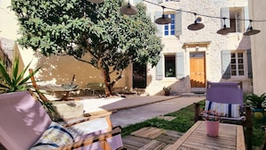 Une cour avec des sièges en plein air, un arbre et un bâtiment doté d’une façade en pierre.