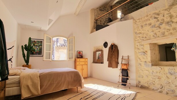 Une chambre avec un lit, un cactus, une armoire, un porte-manteau et un mur en pierre.