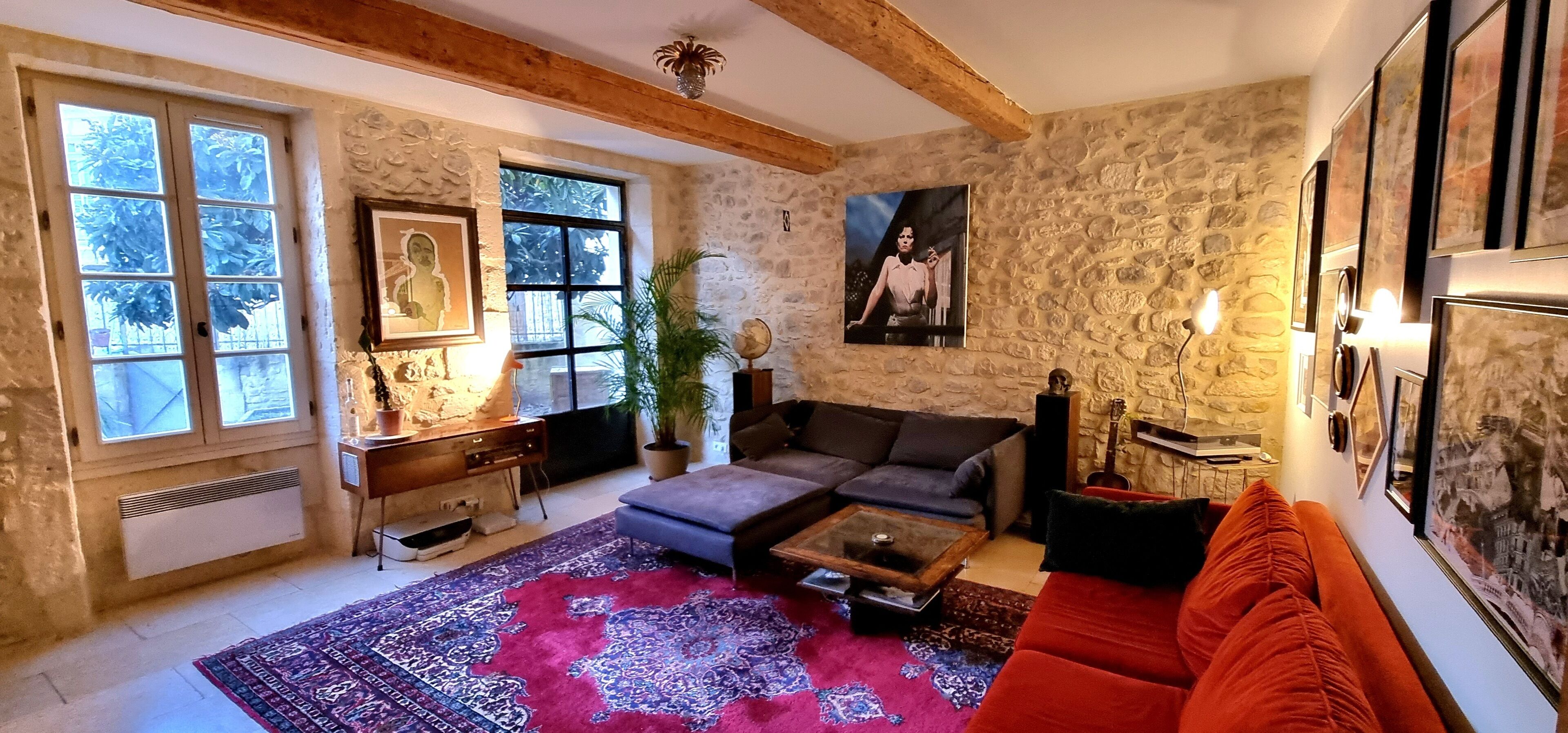 A cozy living room with a stone wall, a large window, a sofa, a coffee table, and a red couch.