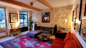 Un salon chaleureux avec un mur en pierre, une grande fenêtre, un canapé, une table basse et un divan rouge.