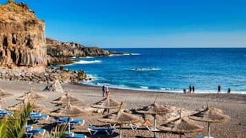 Una spiaggia con ombrelloni, lettini, scogliere rocciose e l'oceano.