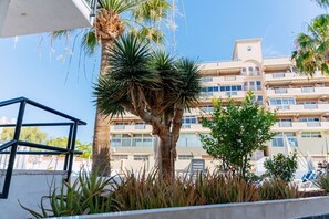 Un immeuble à plusieurs étages, doté de balcons et entouré de palmiers et de diverses plantes.