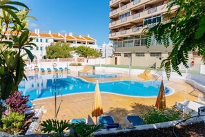 Ein Pool mit Liegestühlen und Sonnenschirmen, umgeben von Gebäuden mit Balkonen.
