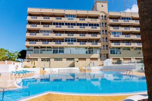 Ein mehrstöckiges Hotel mit Schwimmbad, Balkonen und blauem Himmel.