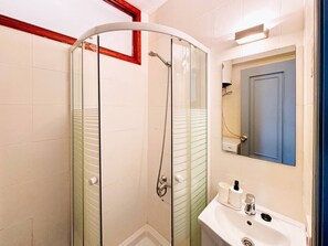 Ein Badezimmer mit einer Duschkabine, einem weißen Waschbecken und einem Spiegel darüber.