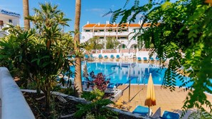Ein Swimmingpool mit Liegestühlen und Sonnenschirmen, umgeben von Palmen und einem Gebäude mit einem Ziegeldach.