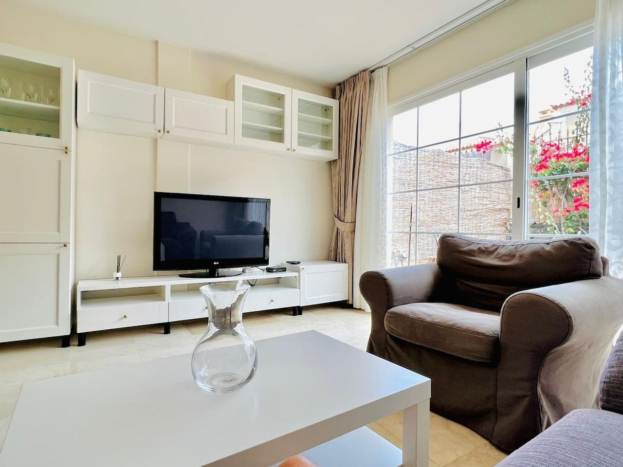 A living room with a flat-screen TV, a sofa, a coffee table, and a cabinet with glass doors.