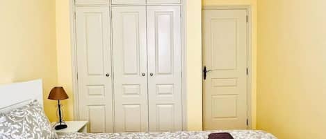 A bedroom with a bed, a ceiling fan, a nightstand, a lamp, and a wardrobe.
