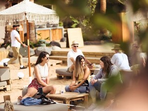 A group of people sitting on wooden benches at a beachside location with umbrellas and lounge chairs in the background.