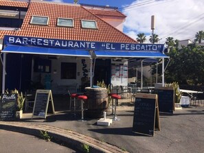 A bar-restaurant with outdoor seating and a sign reading 'BAR-RESTAURANTE 'EL PESCAITO''.