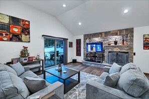 Una sala de estar moderna con chimenea de piedra, un televisor de pantalla plana grande y una zona de estar acogedora con sofás grises y una mesa de centro.