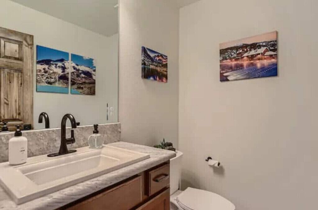 Une salle de bain avec un grand miroir, un lavabo doté d’un robinet noir et trois tableaux encadrés accrochés au mur.