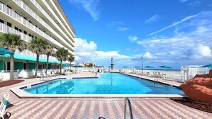 A hotel pool area with a clear blue sky, a large pool, and a building with multiple balconies. - Beachfront Deluxe studio- Ocean Views! (Daytona Beach)