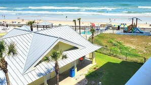 A beach view with a building featuring a sloped roof and a small lawn area. - Beachfront Deluxe studio- Ocean Views! (Daytona Beach)