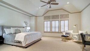 Une chambre à coucher comprenant un lit, une chaise, un bureau, un ventilateur de plafond et de grandes fenêtres équipées de volets.