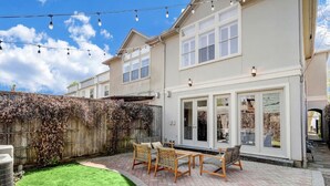 Une maison à deux étages dotée d’un patio comprenant une table et des chaises, un patio couvert et une grande porte-fenêtre coulissante.