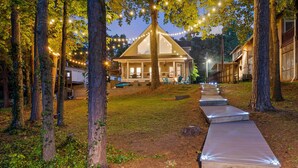 Une maison en bois avec un toit à pignon, entourée d’arbres et dotée d’une terrasse en bois menant à l’entrée.