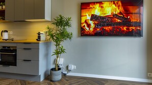 Eine moderne Küche mit Einbauofen, Zimmerpflanze und großem Flachbildfernseher, der ein Feuer zeigt.