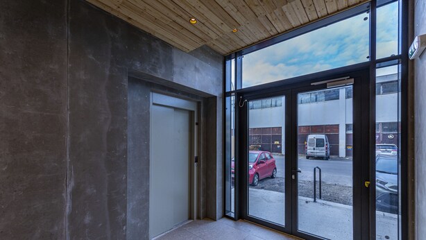 Ein moderner Gebäudeeingang mit Glastür und Holzdecke.