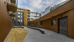 Ein modernes Gebäude mit Innenhof, das eine Mischung aus Holz- und Metallfassaden sowie einen gepflasterten Weg zeigt.