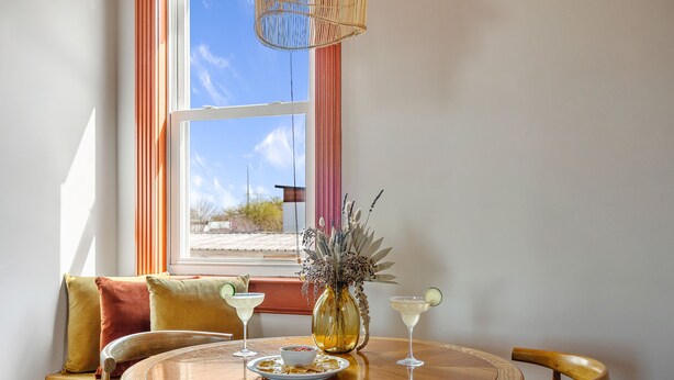 Un comedor con una mesa redonda de madera, dos sillas, un jarrón con flores secas y dos bebidas sobre la mesa.