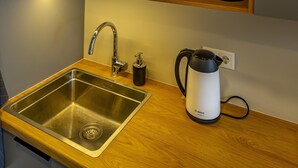 Et køkken med en stålvask, træskabe, en Bosch elkedel og plantetårne på en hylde.