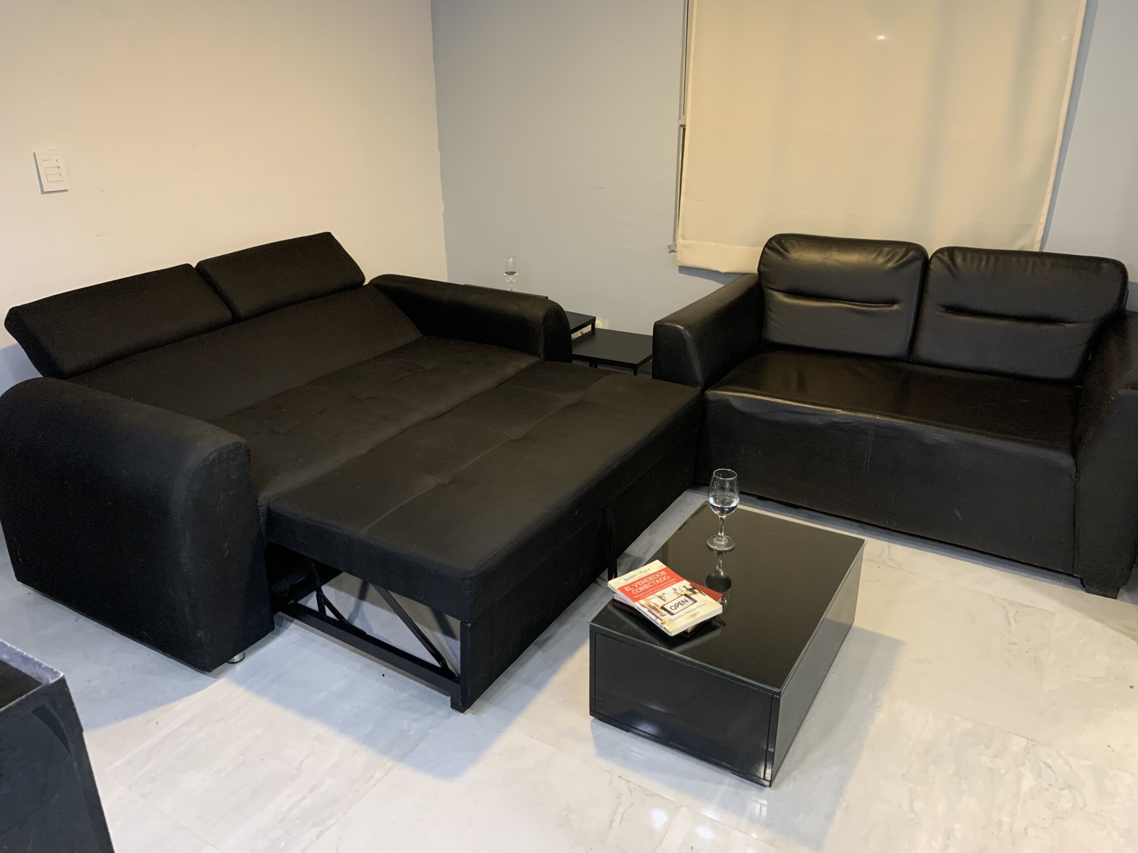 A modern living room with a black sofa, a smaller black armchair, and a glass coffee table with a magazine.