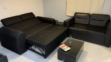 A modern living room with a black sofa, a smaller black armchair, and a glass coffee table with a magazine.