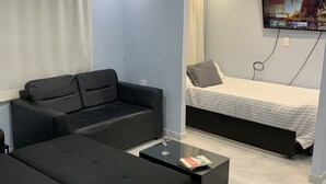 Un espacio habitable moderno y funcional con sofá, mesa de centro, cama y televisor montado en la pared, además de una cortina.
