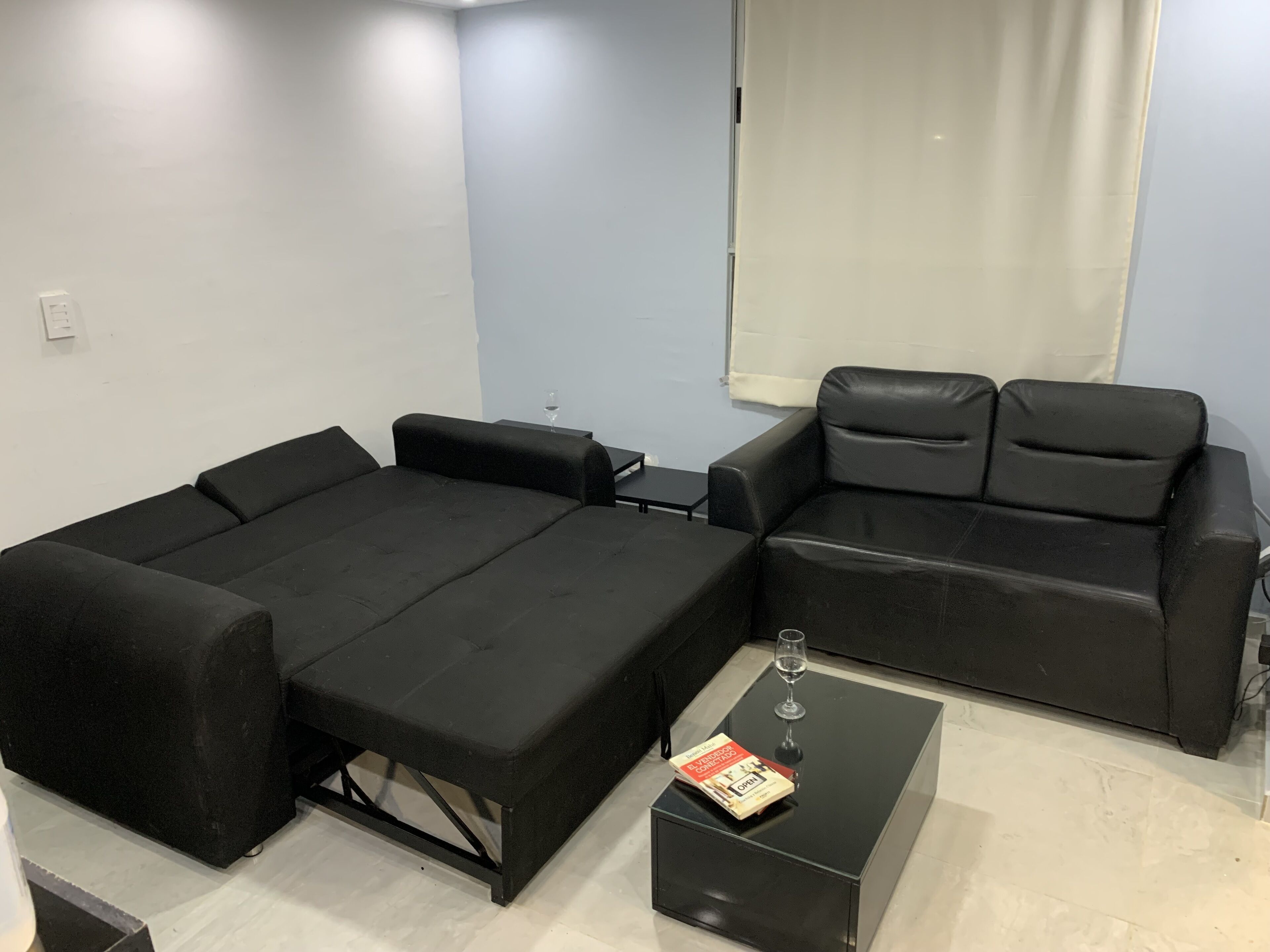 A compact room with a black sofa bed, a small table with a glass of wine, and a book.