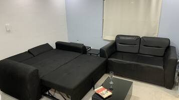 A compact room with a black sofa bed, a small table with a glass of wine, and a book.