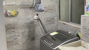 Un baño con pared de piedra, un perchero, una botella de agua y una zona de ducha.