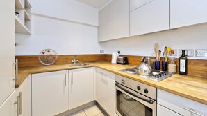 A modern kitchen with white cabinets, a wooden countertop, a sink, a stove, and various kitchen utensils.
