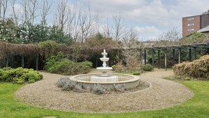A circular garden with a central fountain, surrounded by gravel and grass.