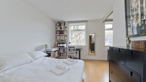 A bedroom with a large bed, a desk, a bookshelf, and a dresser.