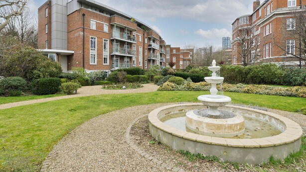 A courtyard with a fountain, surrounded by well-maintained hedges and a gravel path.