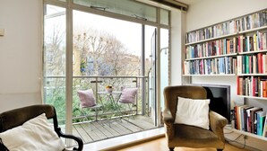A room with a large window, a bookshelf, a television, and two chairs.
