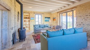 A rustic interior with a stone wall, a fireplace, a blue sofa, and a view through a glass door. - la Corbière - Martigny-le-comte (MARTIGNY-LE-COMTE)