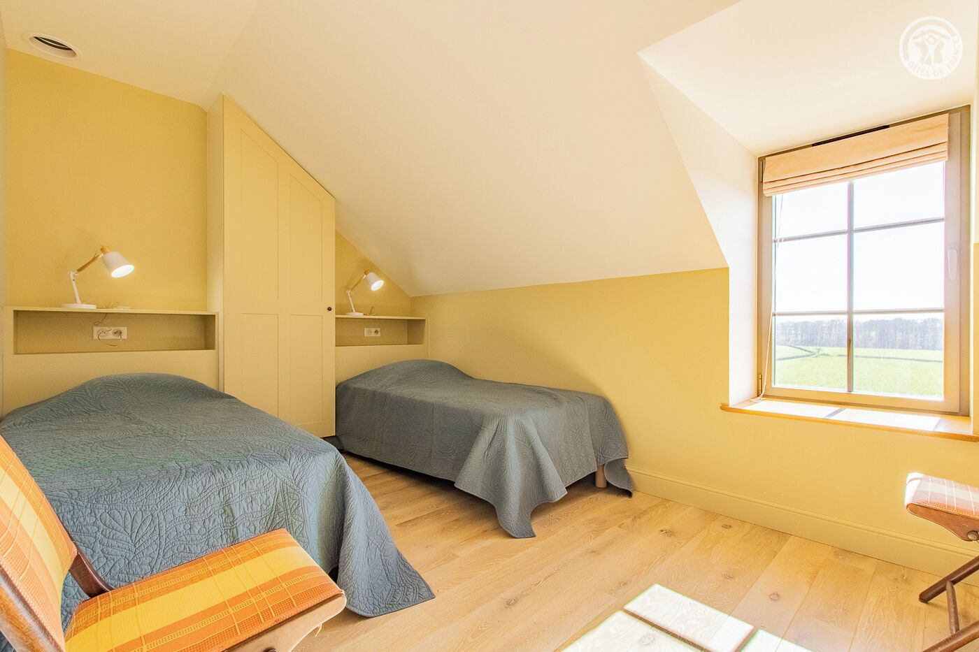 A small, cozy room with two beds, a desk, and a window with a view of a field.