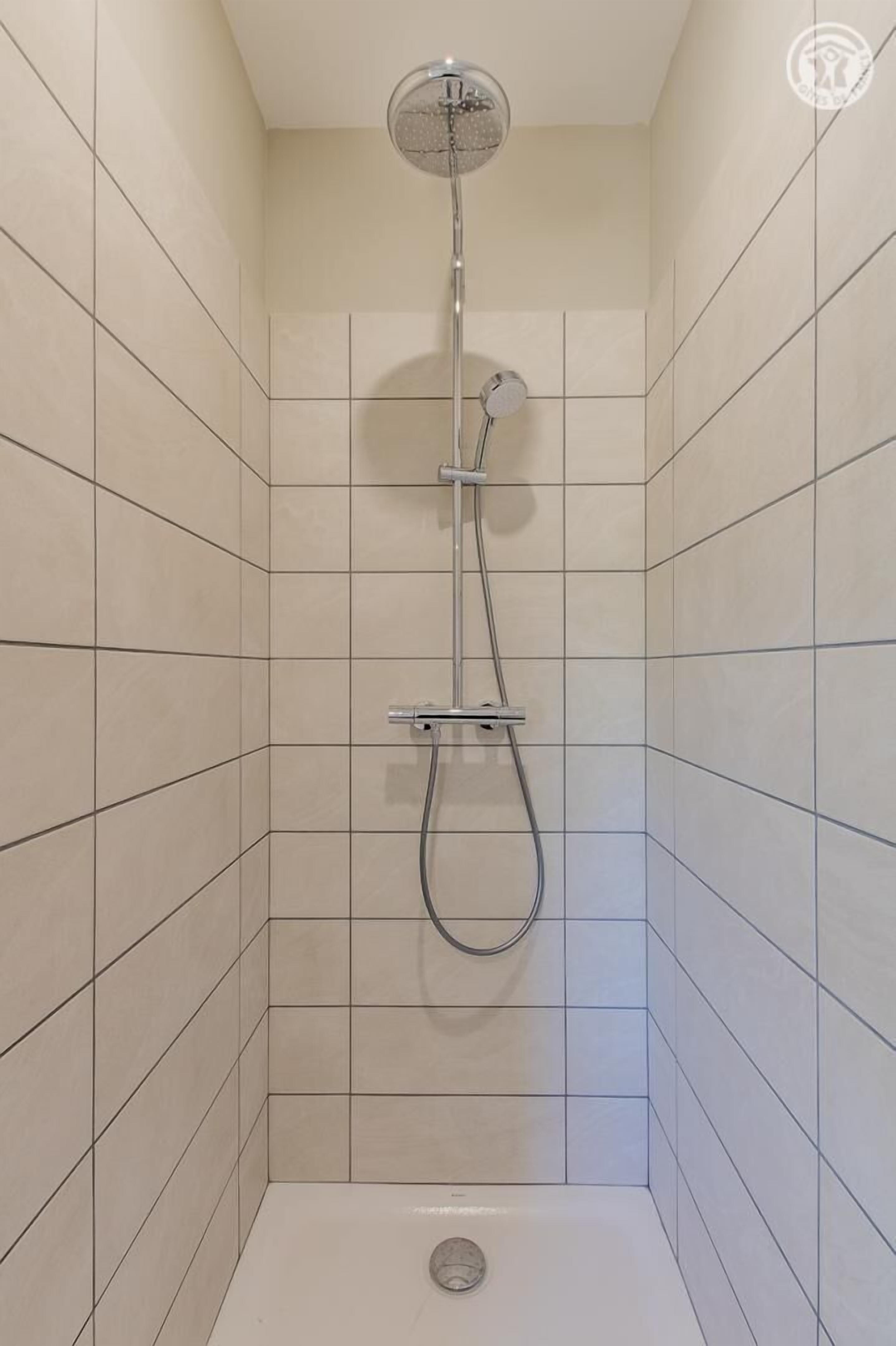 Un vestidor de ducha pequeño con azulejos, un cabezal de ducha de mano y un grifo empotrado.
