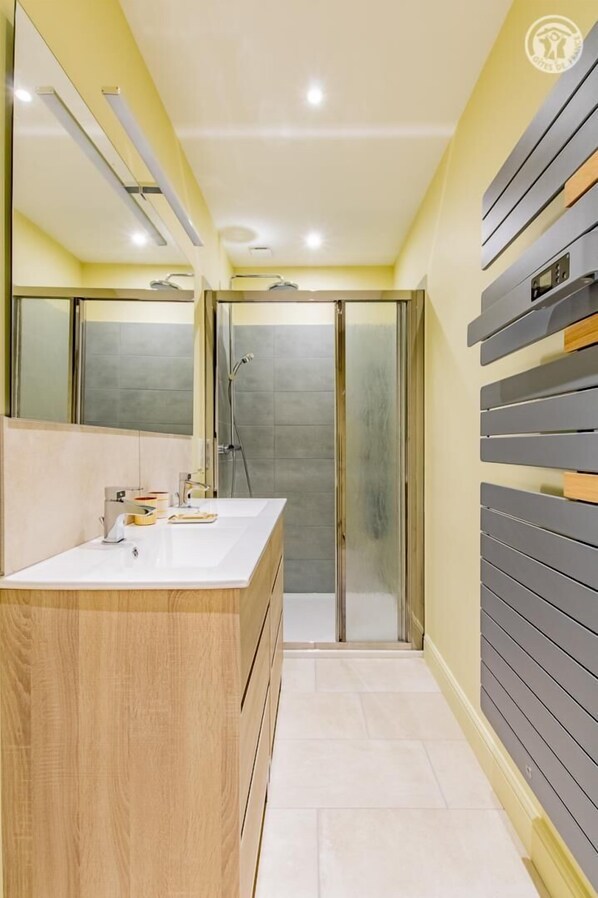 Bathroom features a large mirror, two sinks, a glass shower enclosure, and a tiled floor.