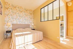 Relax in this serene bedroom with a large bed, a window offering a view of the outside, and a nightstand with a lamp.