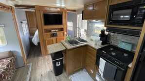 Cocina compacta para autocaravana con estufa, microondas, lavamanos y televisor montado sobre la encimera.