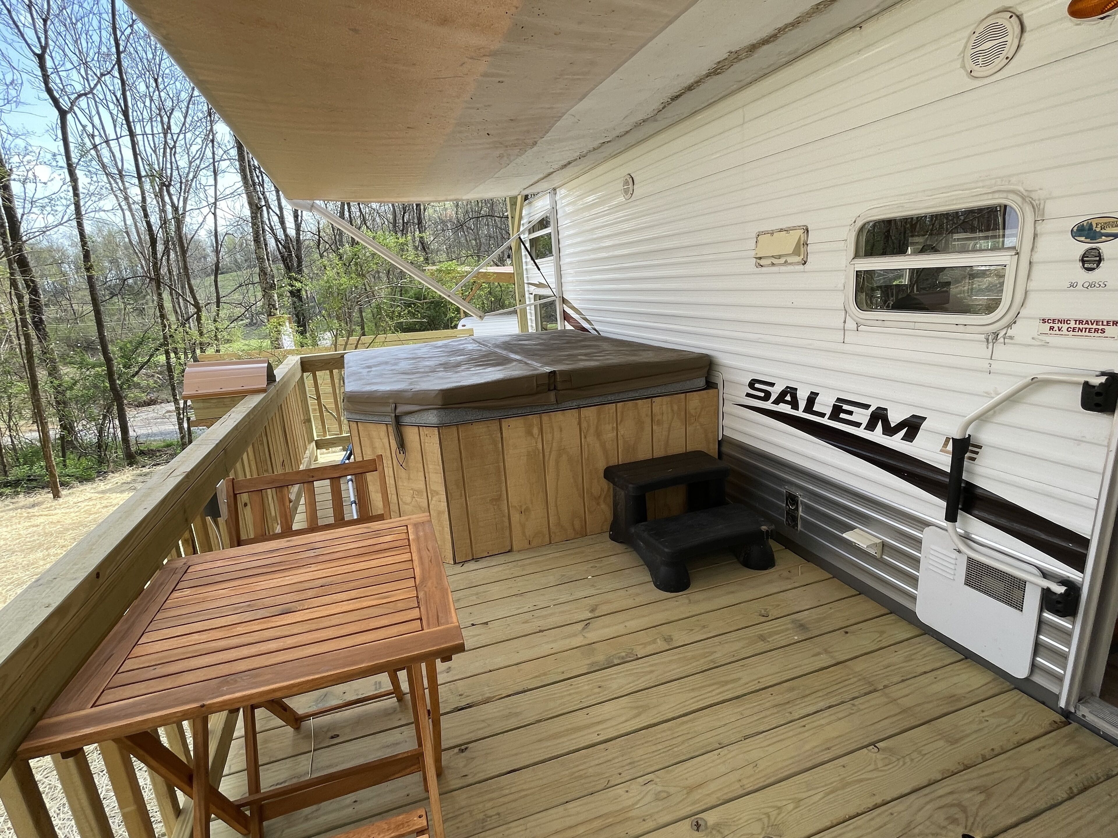 A covered deck with a wooden table and bench, a hot tub, and a white RV with "SALEM" branding.
